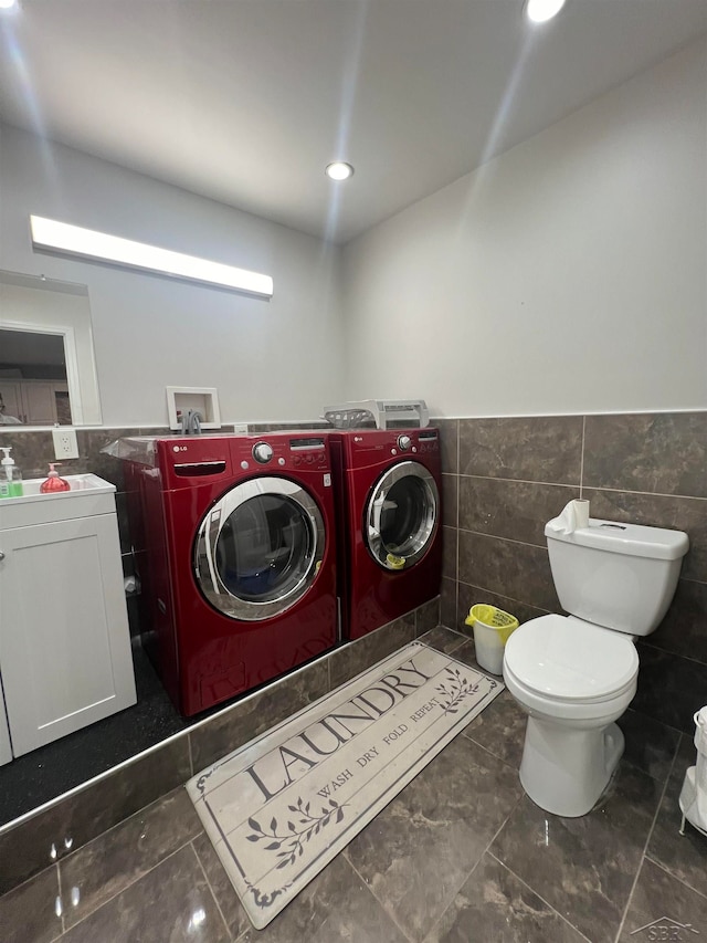 laundry room featuring dark tile patterned flooring, washer and dryer, and tile walls