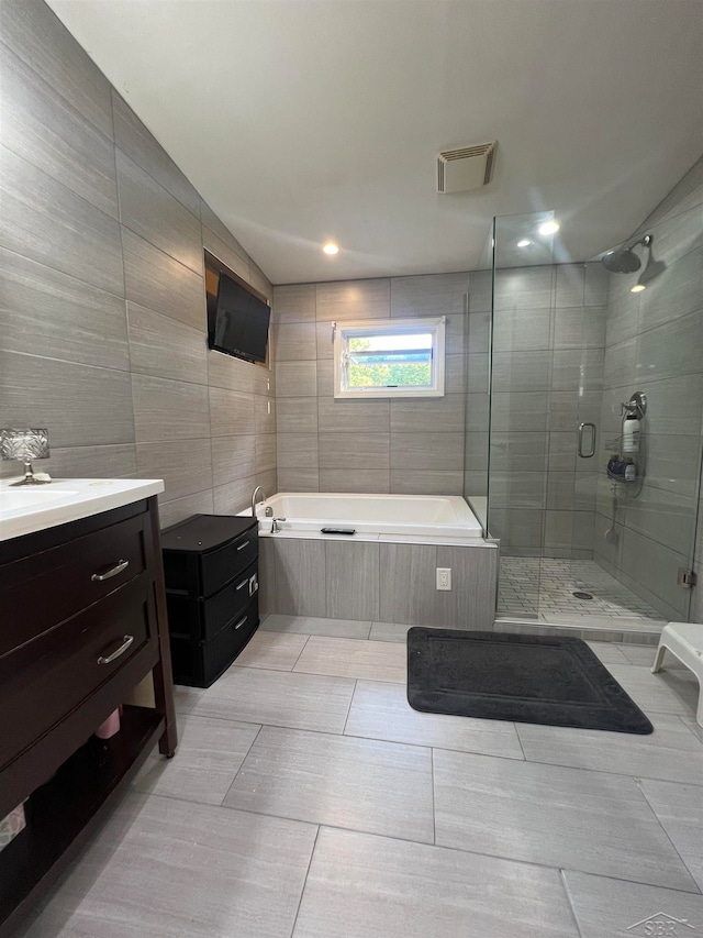 bathroom featuring tile patterned flooring, vanity, independent shower and bath, and tile walls