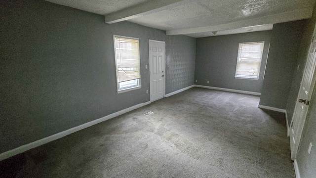 carpeted spare room with beam ceiling, a textured ceiling, and a healthy amount of sunlight