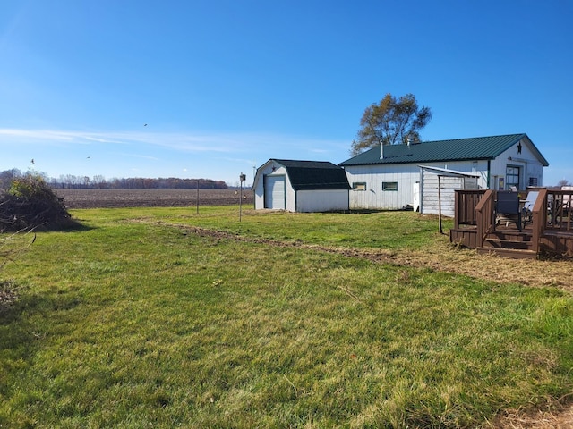 view of yard with a rural view, a garage, an outdoor structure, and a wooden deck