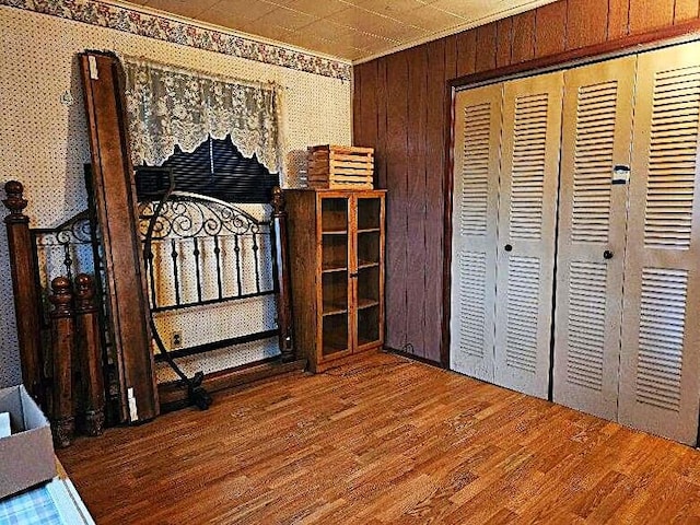 bedroom with crown molding, wood walls, a closet, and wood-type flooring