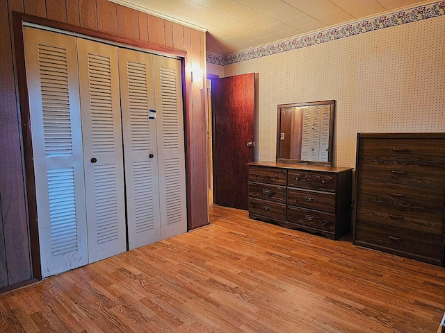 bedroom featuring light hardwood / wood-style floors, wooden walls, and a closet