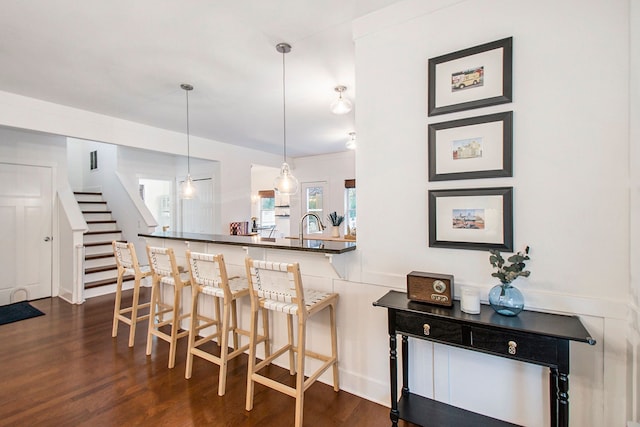 kitchen with sink, hanging light fixtures, dark hardwood / wood-style flooring, kitchen peninsula, and a breakfast bar area