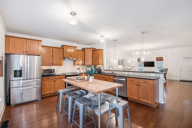 kitchen with a breakfast bar, stainless steel appliances, dark wood-type flooring, sink, and an inviting chandelier