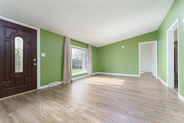 entryway with a textured ceiling, light wood-type flooring, and vaulted ceiling