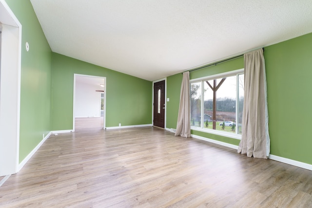 unfurnished room featuring lofted ceiling, a textured ceiling, and light hardwood / wood-style flooring