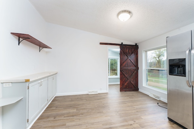 unfurnished dining area featuring a textured ceiling, a barn door, light hardwood / wood-style floors, and lofted ceiling