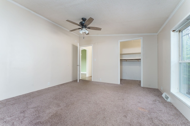 unfurnished bedroom featuring ornamental molding, a textured ceiling, light colored carpet, ceiling fan, and a closet