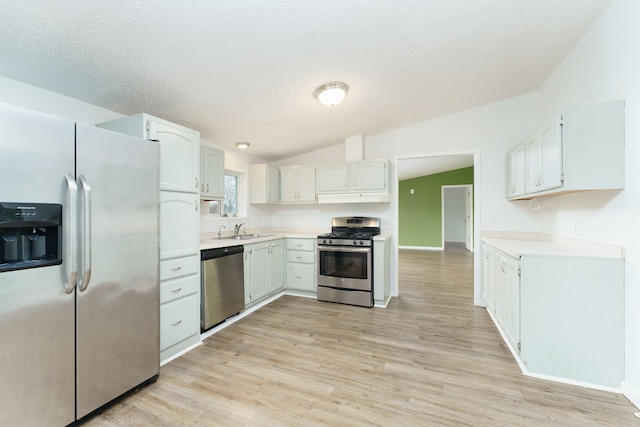 kitchen featuring lofted ceiling, sink, light wood-type flooring, white cabinetry, and stainless steel appliances