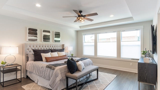 bedroom with a tray ceiling, multiple windows, ceiling fan, and dark hardwood / wood-style flooring