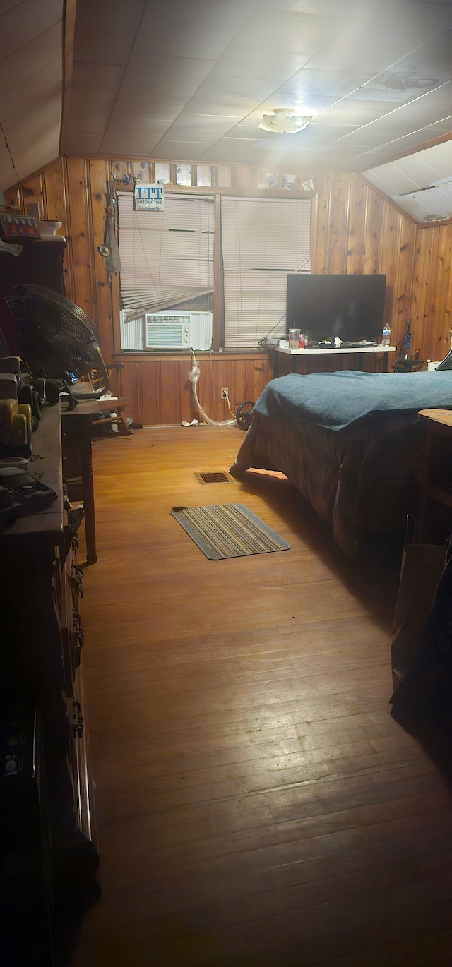 bedroom with hardwood / wood-style floors, wooden walls, cooling unit, and lofted ceiling