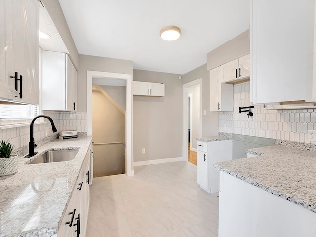 kitchen with backsplash, white cabinetry, sink, and light stone countertops