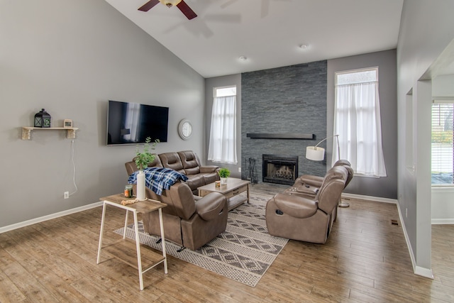 living room with a stone fireplace, ceiling fan, high vaulted ceiling, and light hardwood / wood-style floors