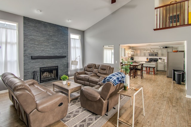 living room featuring a fireplace, light wood-type flooring, high vaulted ceiling, and ceiling fan