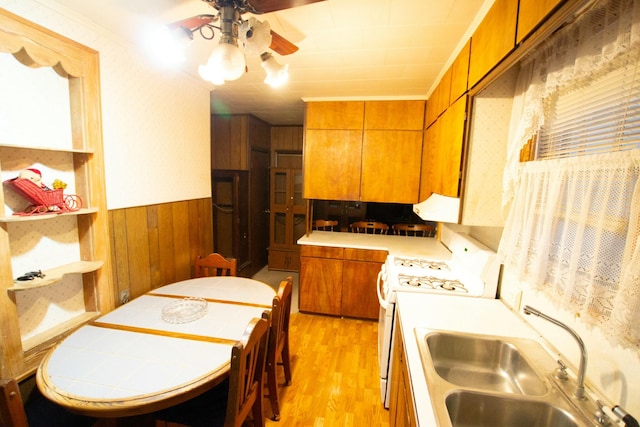 kitchen with ceiling fan, wooden walls, sink, electric stove, and light hardwood / wood-style floors