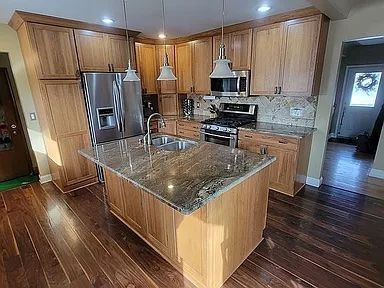 kitchen featuring sink, stainless steel appliances, dark hardwood / wood-style floors, pendant lighting, and a kitchen island with sink