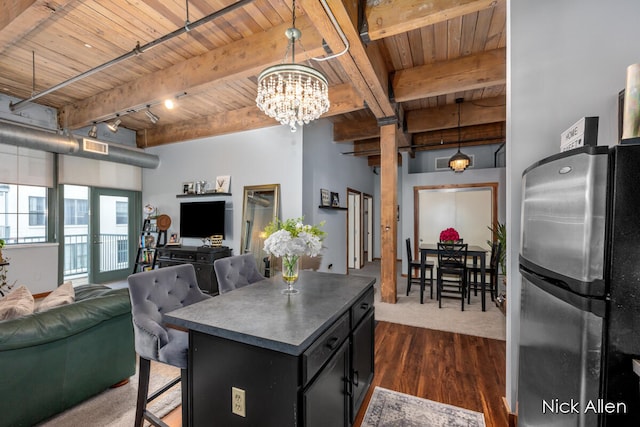 kitchen with hanging light fixtures, stainless steel fridge, beam ceiling, a kitchen island, and wood ceiling