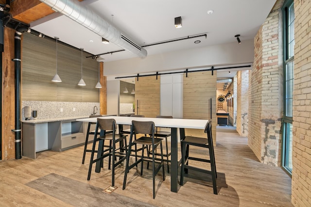 dining space with a barn door, light hardwood / wood-style flooring, and brick wall