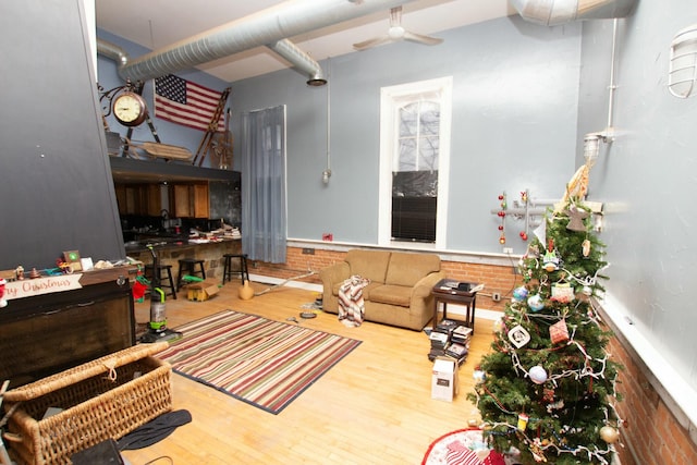 living room with ceiling fan, hardwood / wood-style floors, and brick wall