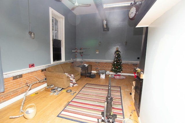 interior space with wood-type flooring, ceiling fan, and brick wall