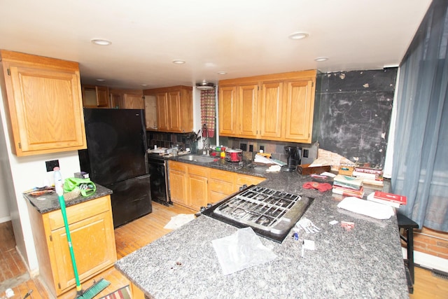 kitchen featuring sink, light hardwood / wood-style floors, tasteful backsplash, and black appliances