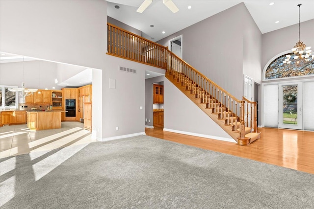 unfurnished living room featuring light hardwood / wood-style flooring, a towering ceiling, and ceiling fan with notable chandelier