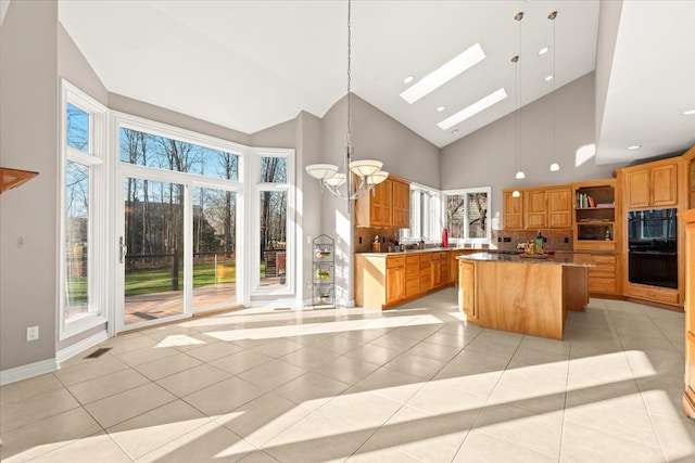 kitchen with backsplash, high vaulted ceiling, a center island, hanging light fixtures, and light tile patterned flooring