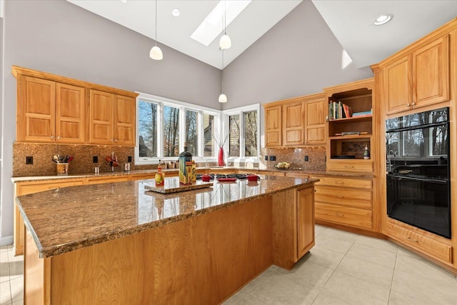 kitchen with a center island, dark stone counters, a skylight, double oven, and decorative light fixtures