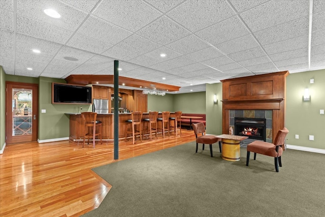 living room featuring bar, a tiled fireplace, a paneled ceiling, and hardwood / wood-style flooring