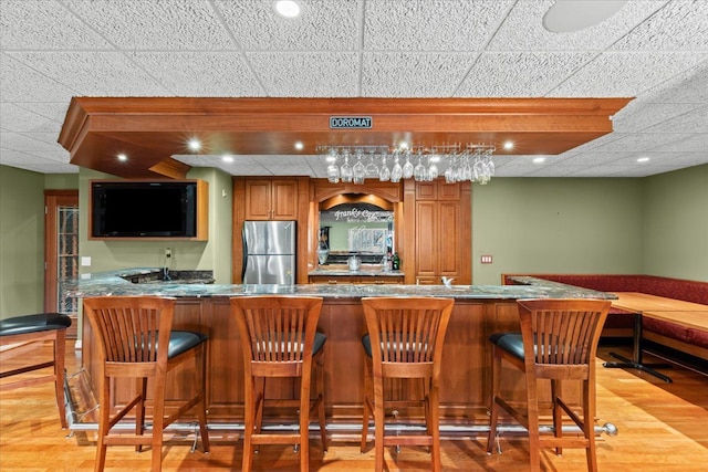 bar featuring light wood-type flooring, stainless steel refrigerator, and a paneled ceiling