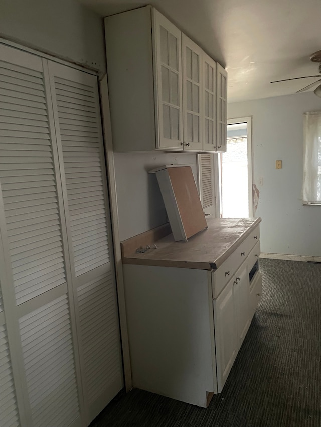 kitchen with ceiling fan, white cabinets, and dark colored carpet