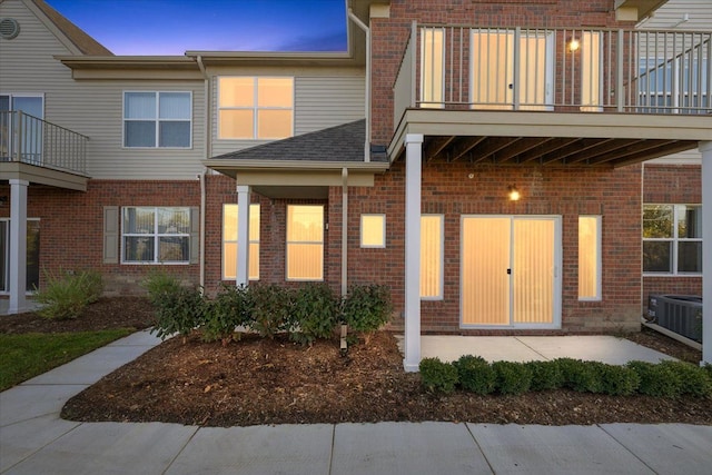 exterior entry at dusk featuring central AC and a balcony