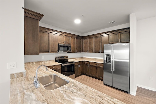 kitchen with sink, light hardwood / wood-style flooring, light stone countertops, appliances with stainless steel finishes, and dark brown cabinets