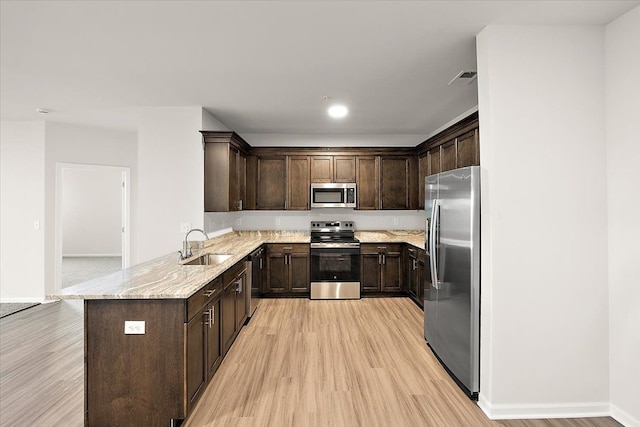 kitchen with kitchen peninsula, light stone counters, dark brown cabinets, stainless steel appliances, and light hardwood / wood-style floors