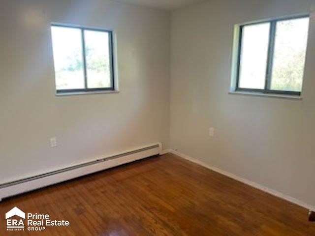 empty room featuring dark wood-type flooring and a baseboard radiator