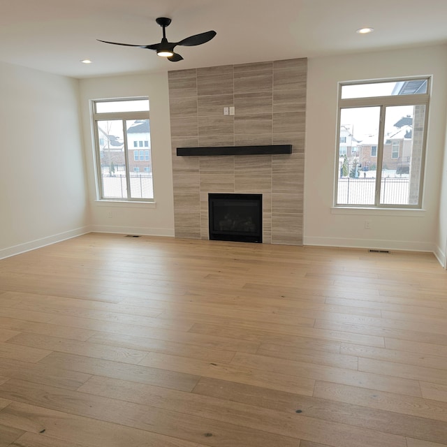 unfurnished living room featuring light wood-type flooring, a tiled fireplace, and ceiling fan