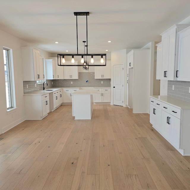 kitchen featuring a kitchen island, sink, hanging light fixtures, light wood-type flooring, and white cabinets