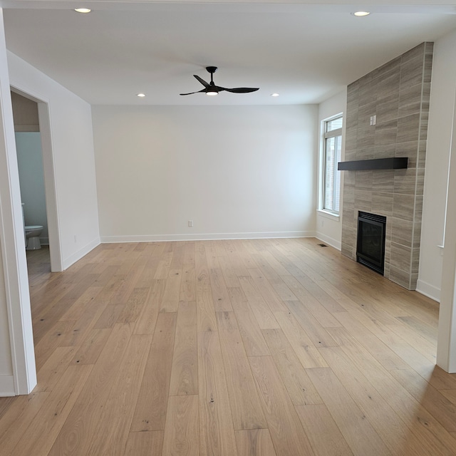 unfurnished living room with light hardwood / wood-style floors, ceiling fan, and a tiled fireplace