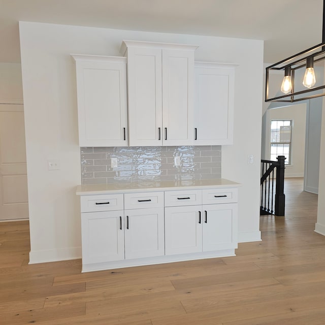 kitchen featuring light wood-type flooring, white cabinetry, tasteful backsplash, and decorative light fixtures