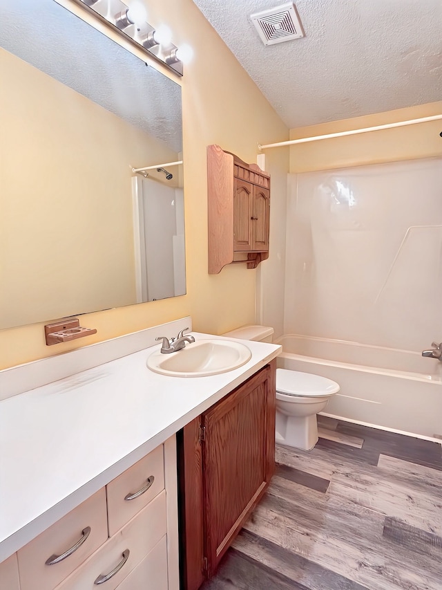 full bathroom with washtub / shower combination, hardwood / wood-style floors, a textured ceiling, toilet, and vanity