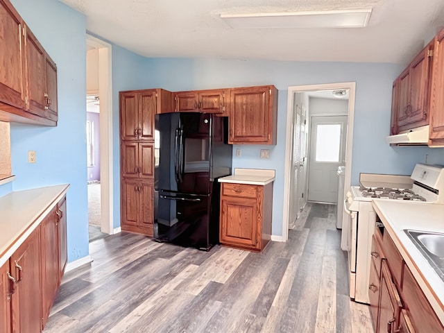 kitchen featuring light wood-type flooring, white gas range oven, black fridge, vaulted ceiling, and sink