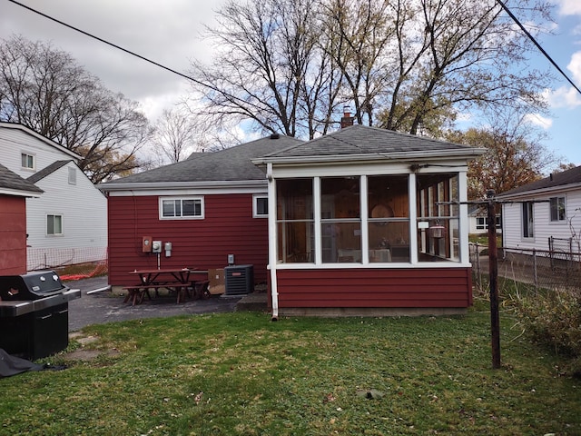 rear view of house with a sunroom, central AC unit, and a lawn