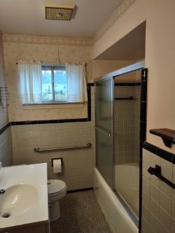 full bathroom featuring combined bath / shower with glass door, vanity, toilet, and tile walls