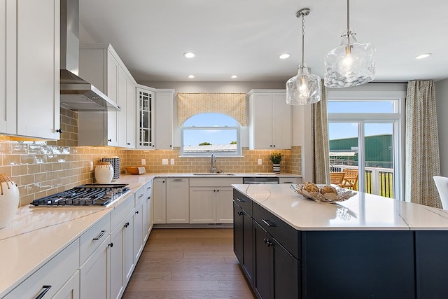 kitchen featuring wall chimney exhaust hood, stainless steel gas cooktop, pendant lighting, light hardwood / wood-style flooring, and white cabinets