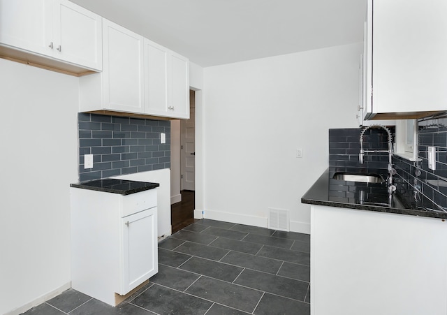 kitchen with dark stone counters, sink, decorative backsplash, dark tile patterned floors, and white cabinetry