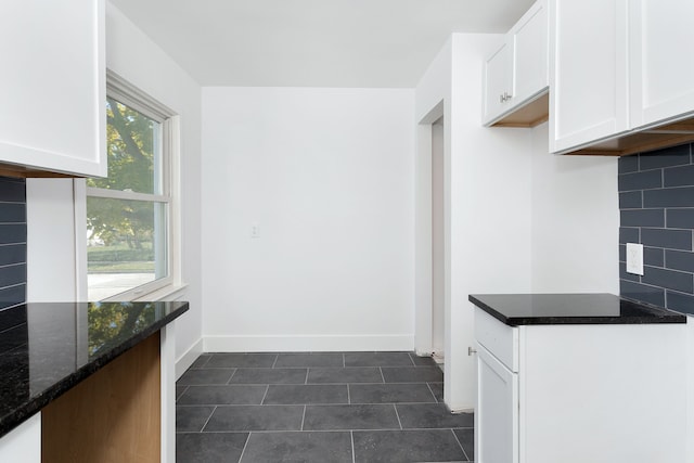 kitchen with dark tile patterned flooring, white cabinetry, backsplash, and dark stone counters