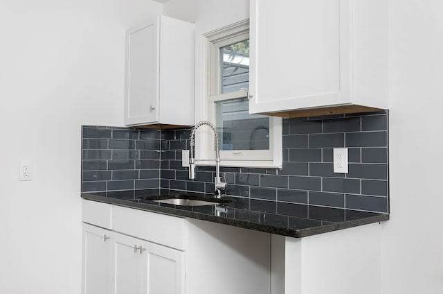 kitchen featuring sink, backsplash, white cabinetry, and dark stone countertops