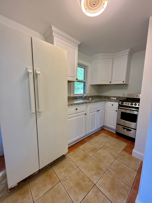 kitchen with sink, stainless steel stove, light tile patterned floors, white fridge, and white cabinets