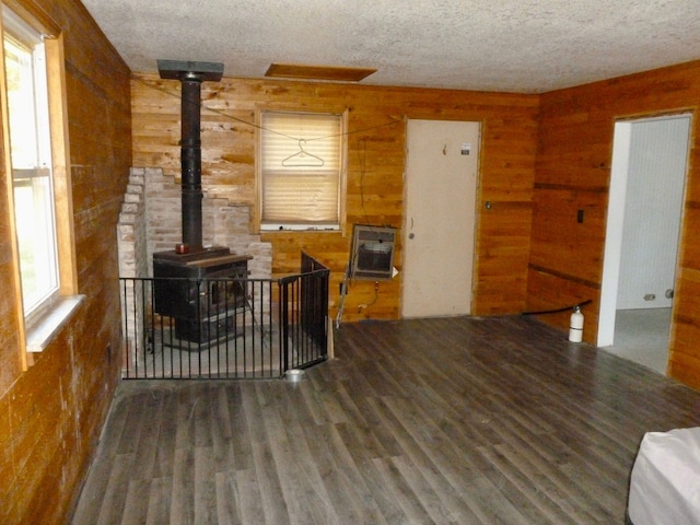 living room with a textured ceiling, dark hardwood / wood-style flooring, heating unit, and a wood stove