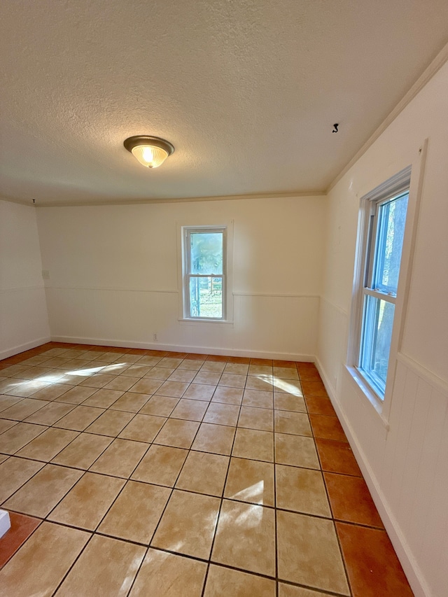 spare room with light tile patterned flooring, ornamental molding, and a textured ceiling